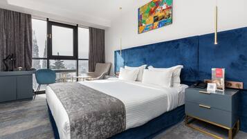 Ein modernes Hotelzimmer mit einem großen Bett, einem Schreibtisch, einem Sessel und Blick auf die Stadt.