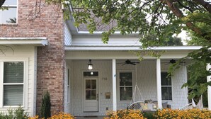 Une maison à la façade en briques, avec un porche blanc et un chemin de pierre menant à l’entrée.