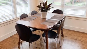 Une salle à manger avec une table en bois, des chaises noires, une plante en pot et un luminaire suspendu.