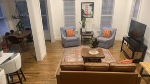 Un salon spacieux avec un canapé en cuir marron, deux fauteuils, une table à manger et un téléviseur.