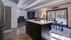 Una cucina moderna con isola centrale, zona pranzo con tavolo e sedie, e vista sull'esterno attraverso ampie finestre.
