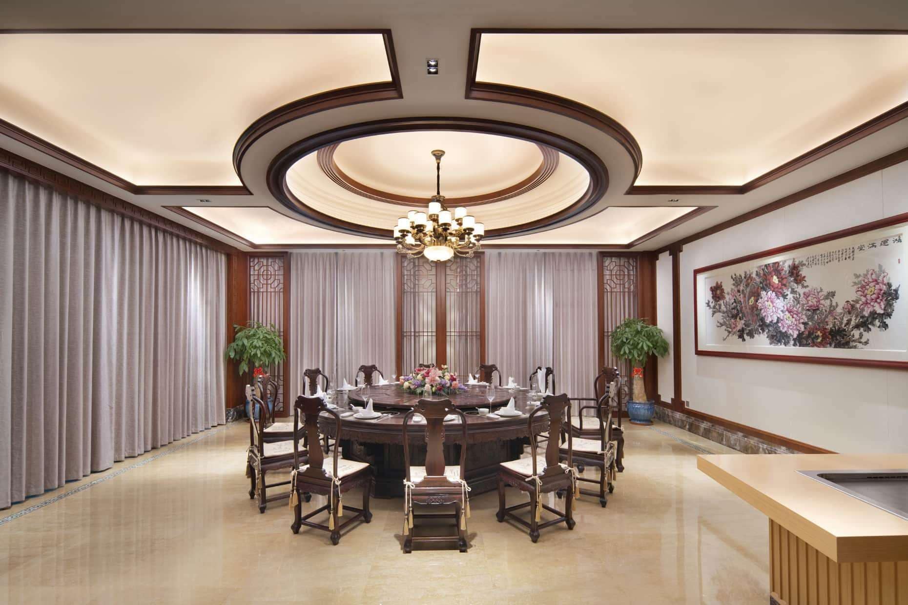 A formal dining room with a round table, chairs, a chandelier, and a painting on the wall.
