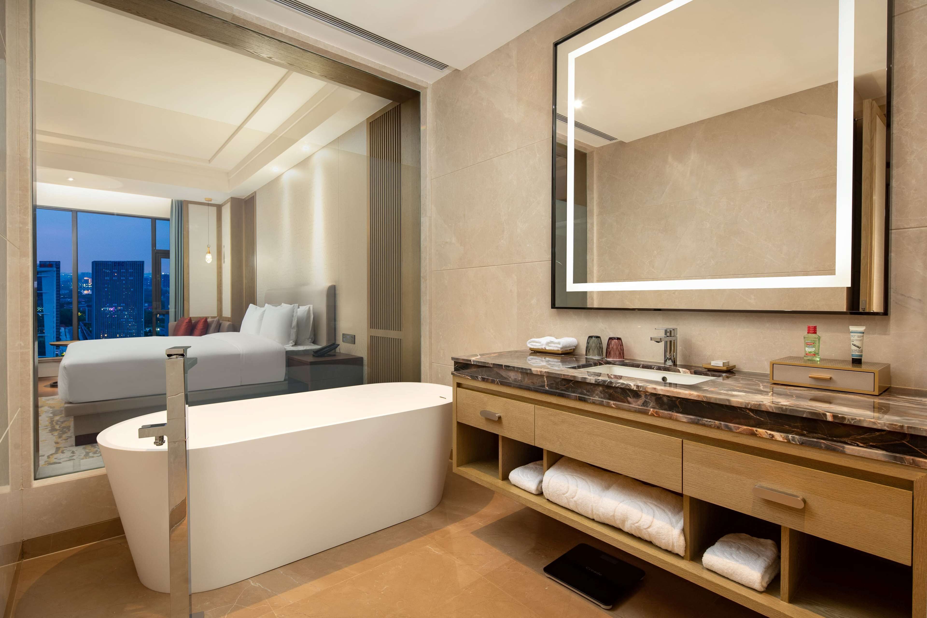 A modern bathroom with a large mirror, a bathtub, and a vanity with a marble countertop.
