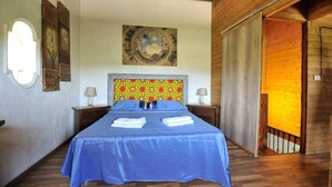 Une chambre à coucher avec un grand lit, deux tables de chevet, une tête de lit ornée d’un motif coloré et un tableau au-dessus du lit.
