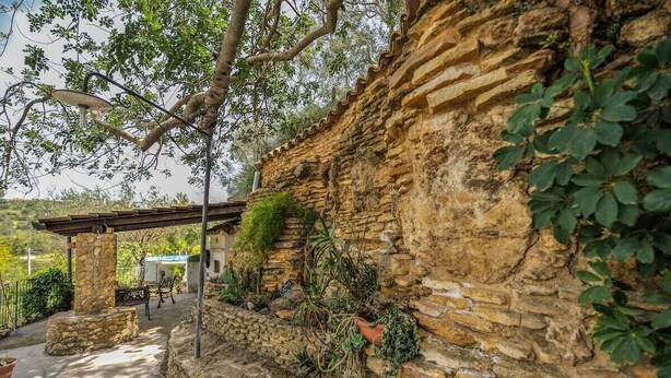Un mur de pierre recouvert de plantes grimpantes, une pergola et un espace de détente extérieur de style rustique.