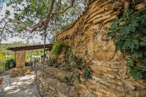 A stone wall with climbing plants, a pergola, and a rustic outdoor seating area. - Villa carrubbo (Pietraperzia)