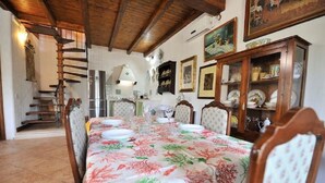 Un coin repas avec une longue table dressée pour six personnes, des chaises en bois, un escalier et un buffet contenant de la vaisselle.