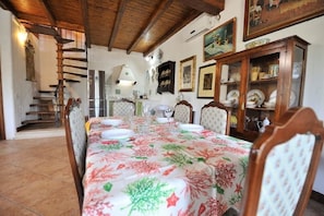 A dining area with a long table set for six, wooden chairs, a staircase, and a cabinet with dishes.