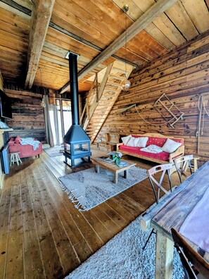 A log cabin interior with a wooden floor, a sofa, a table, and a wood-burning stove. - Grange de Marius - Authentic Savoyard barn (Albiez-Montrond)