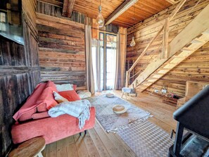 A rustic wooden interior with a red sofa, a woven rug, and a staircase. - Grange de Marius - Authentic Savoyard barn (Albiez-Montrond)