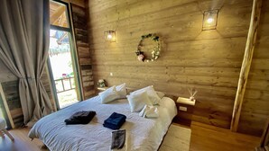 A wooden-paneled bedroom with a bed, pillows, a bedside table, and a wall-mounted light fixture. - Grange de Marius - Authentic Savoyard barn (Albiez-Montrond)