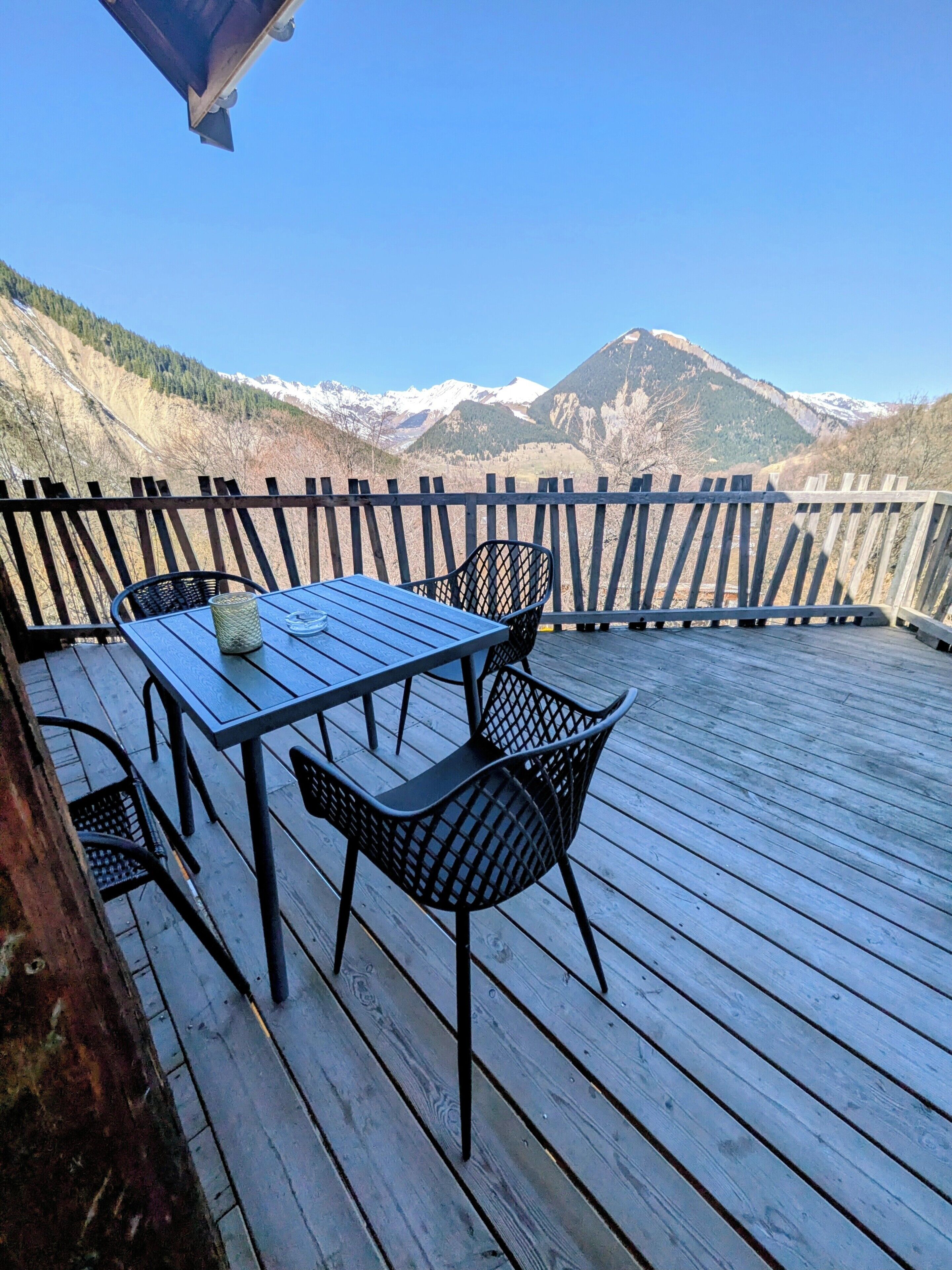 Une terrasse en bois avec une table et des chaises, offrant une vue sur un paysage montagneux.