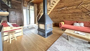 A cozy log cabin interior with a central wood-burning stove, wooden walls, a red sofa, and a wooden bench. - Grange de Marius - Authentic Savoyard barn (Albiez-Montrond)