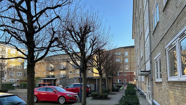 A residential area with parked cars, a sidewalk lined with trees, and multi-story buildings in the background. - Large Shoreditch, Hoxton 3-bed Garden Flat (London)