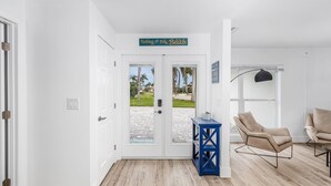 Ein Hotel Eingang mit einem Schild, auf dem 'Nothing to Fear Beach' steht, einem blauen Beistelltisch, zwei beige Sesseln und Blick auf den Strand durch Glastüren.