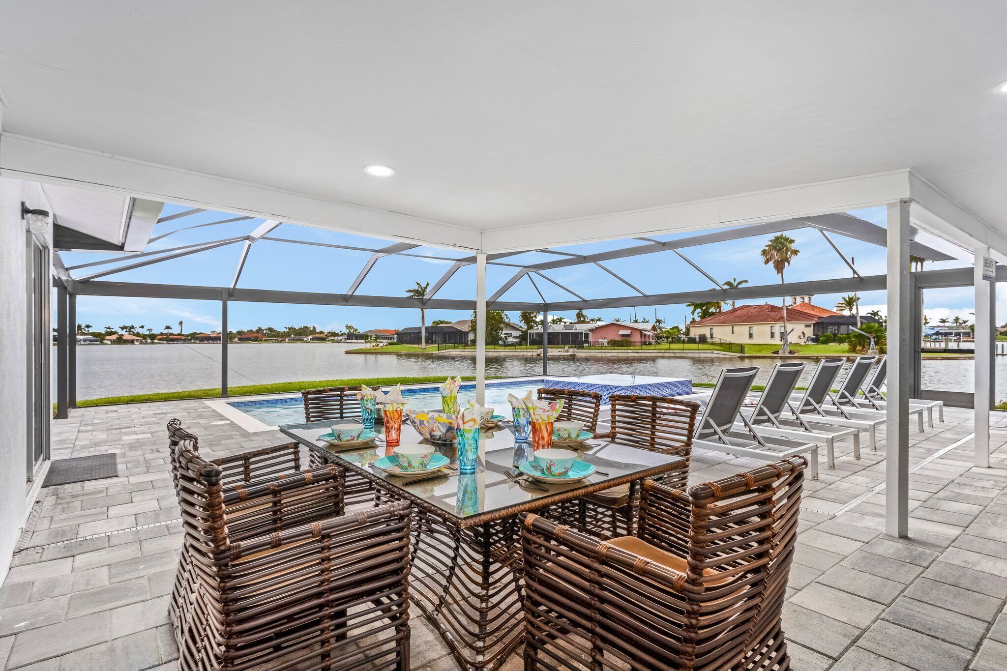 A covered outdoor area with a pool, lounge chairs, and a dining table with chairs.