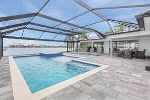 A swimming pool with a glass ceiling, surrounded by lounge chairs and a view of the water. - Villa Soleada | Gulf-Access, Heated Pool & Spa (Cape Coral)