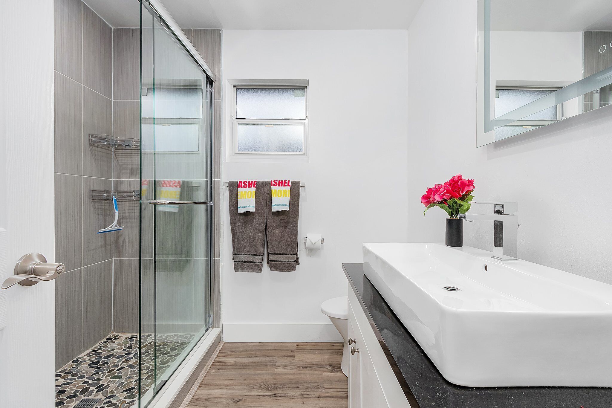 A modern bathroom with a glass shower enclosure, a white sink, and a mirror above the sink.