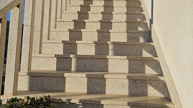 A set of stone steps leading to a door with a decorative arch, flanked by a railing and a planter with greenery at the bottom.