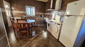 A kitchen with a dining table, chairs, a washing machine, a microwave, and a refrigerator.