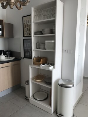 A modern kitchen with white cabinetry, a built-in shelf unit, and a trash bin.