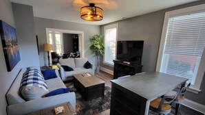 A modern living room with a sofa, coffee table, TV, and a dining area with chairs.
