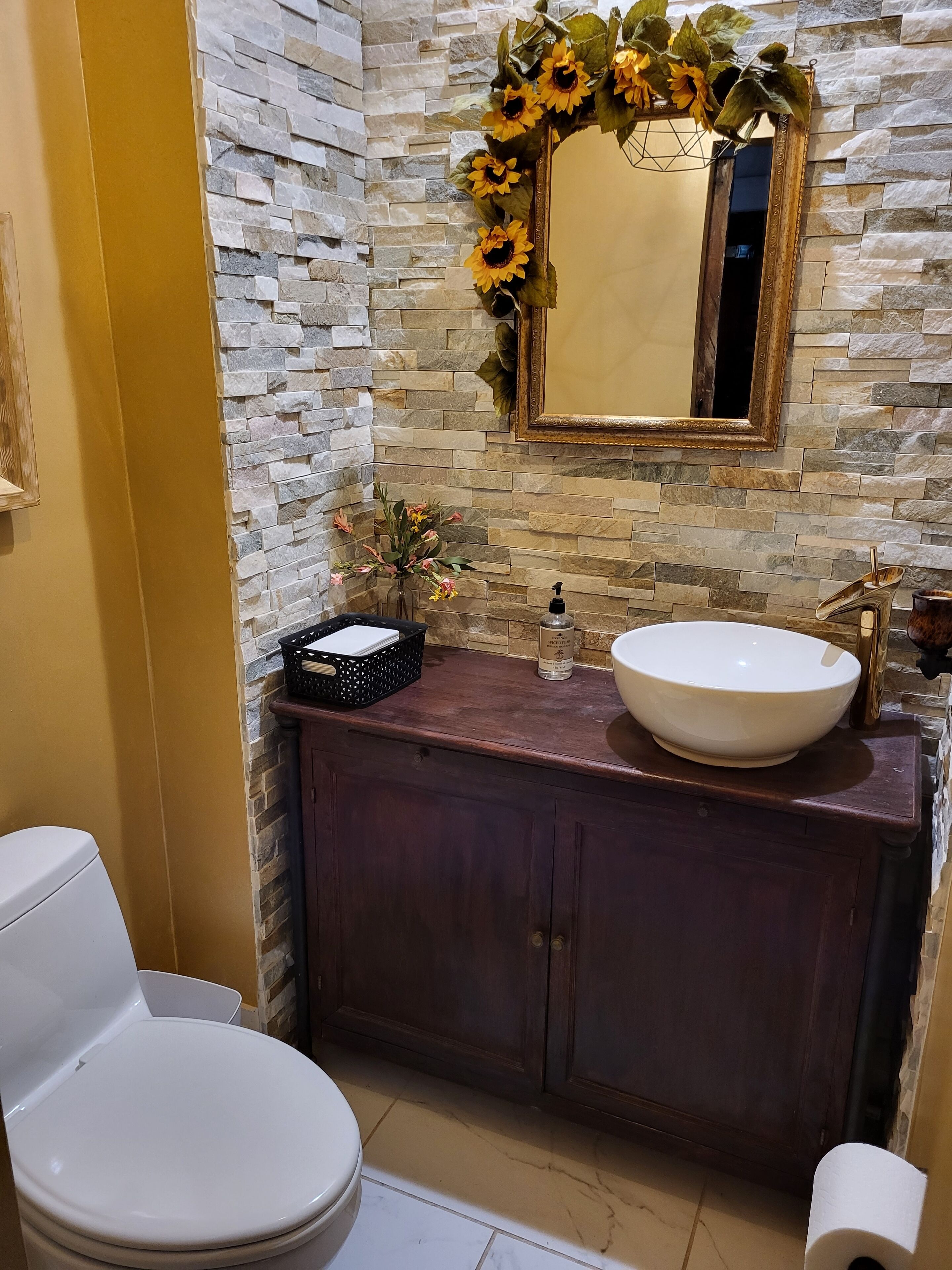 A bathroom with a stone wall, a white sink, a wooden vanity, and a toilet.