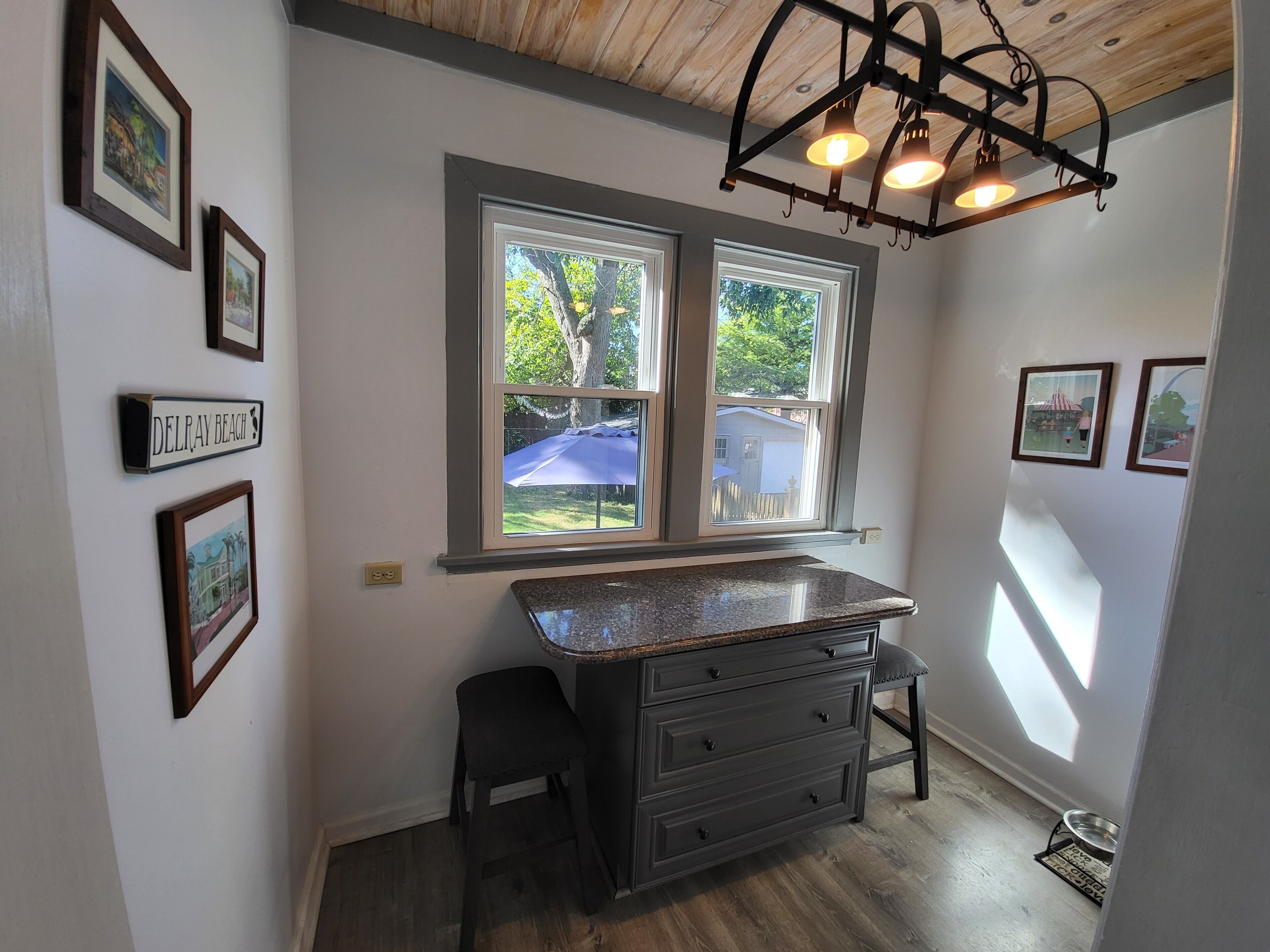 A kitchen with a granite countertop, two windows, and a pendant light fixture.