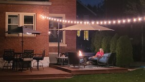 An outdoor patio with a fire pit, outdoor furniture, and string lights.