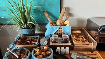 A breakfast buffet with croissants, bread, jams, and utensils.