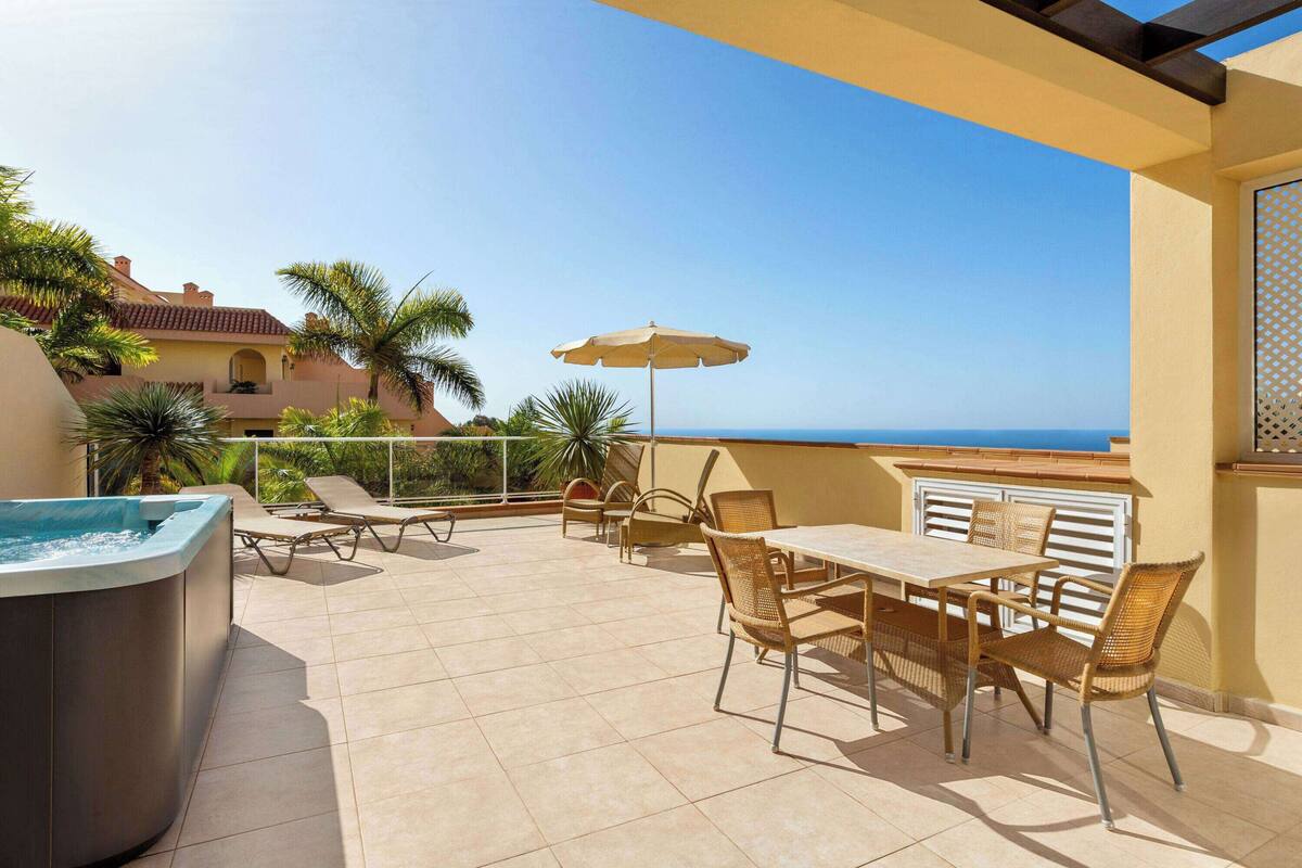 A rooftop terrace with a hot tub, lounge chairs, and a table with chairs.