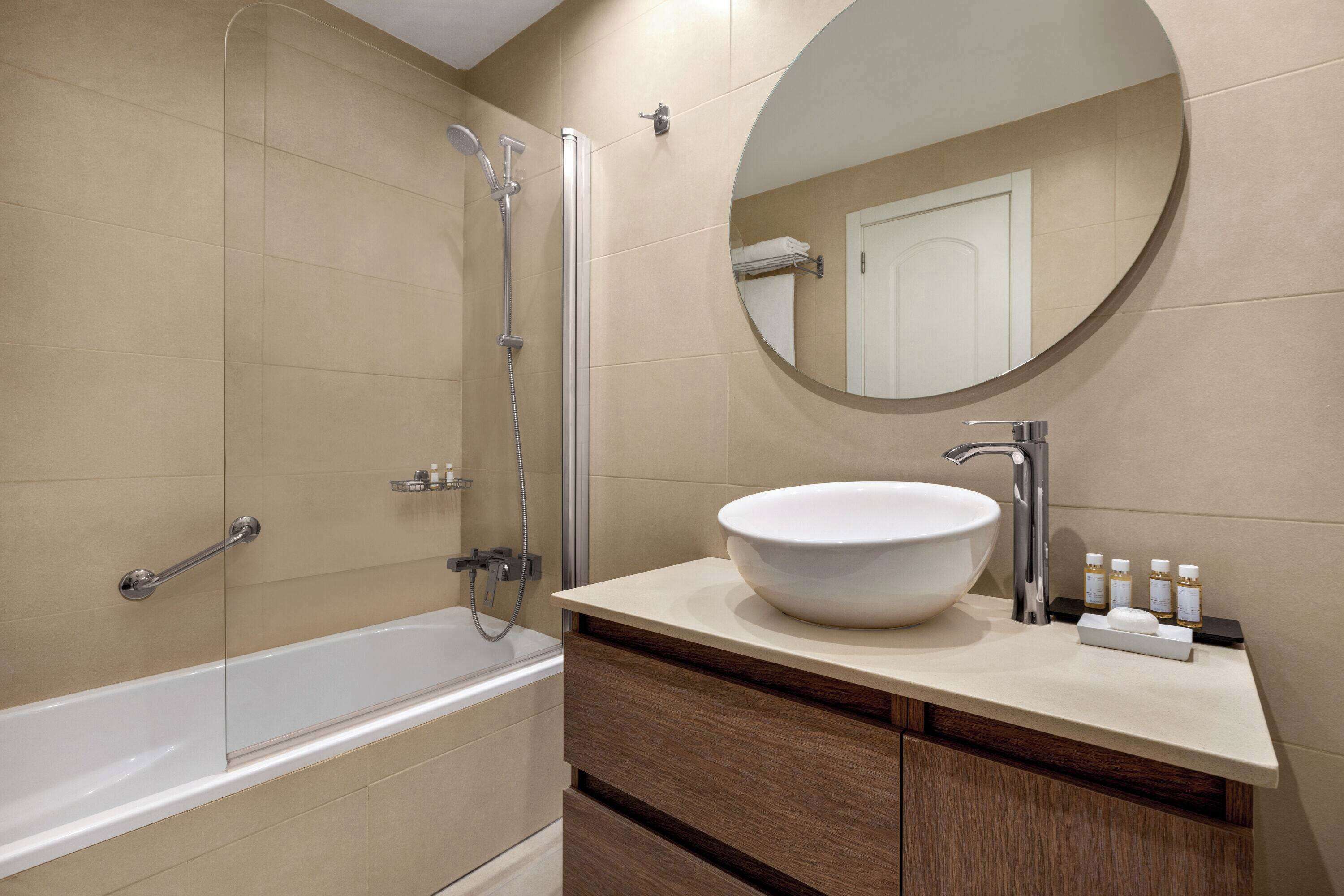 A modern bathroom with a bathtub, a round mirror, and a sink with toiletries.