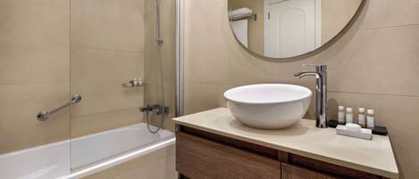 A modern bathroom with a bathtub, a round mirror, and a sink with toiletries.