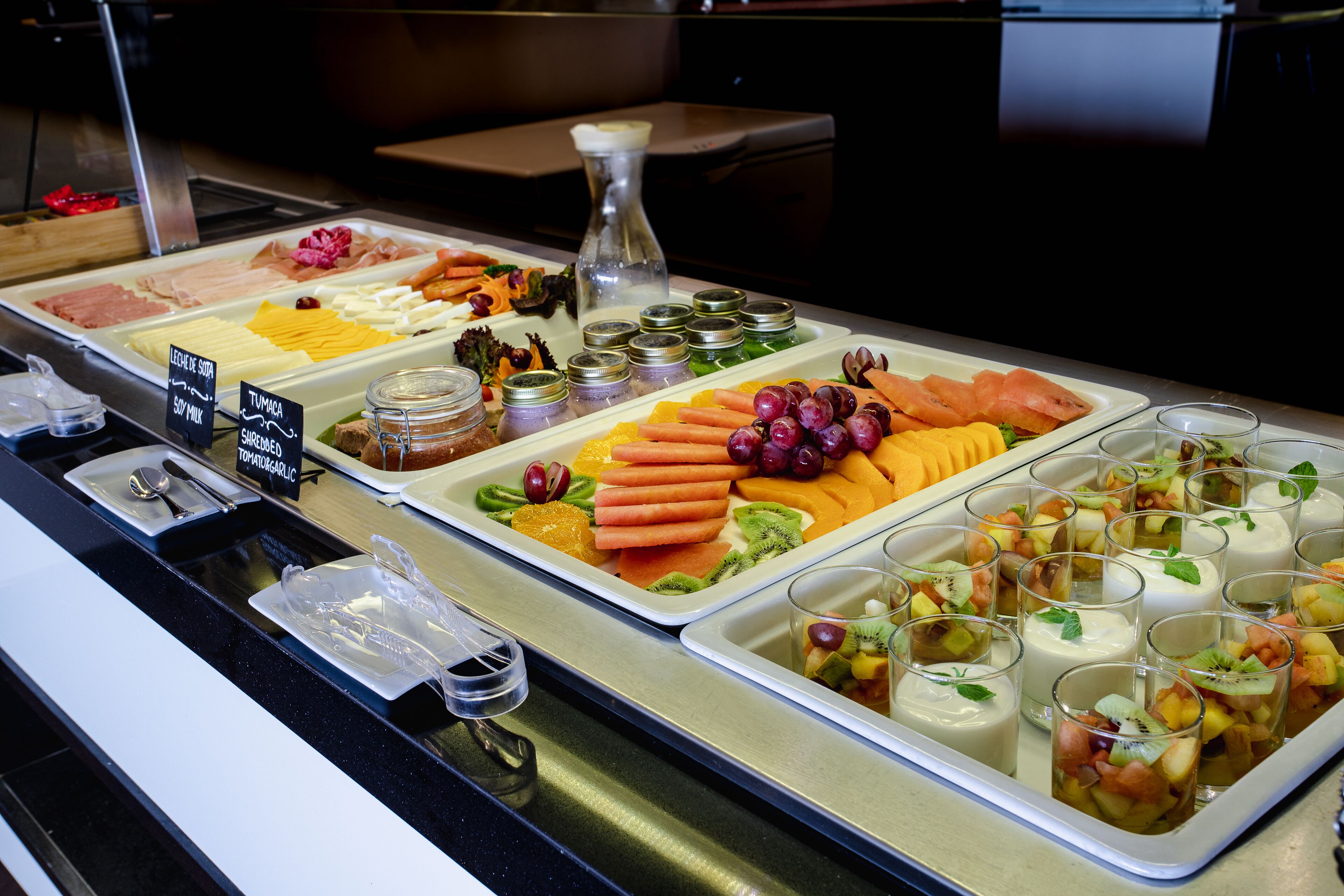 A buffet with various food items including meats, cheeses, fruits, and yogurt parfaits.