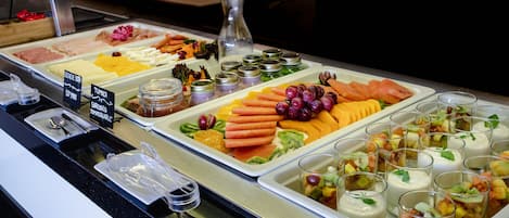 A buffet with various food items including meats, cheeses, fruits, and yogurt parfaits.