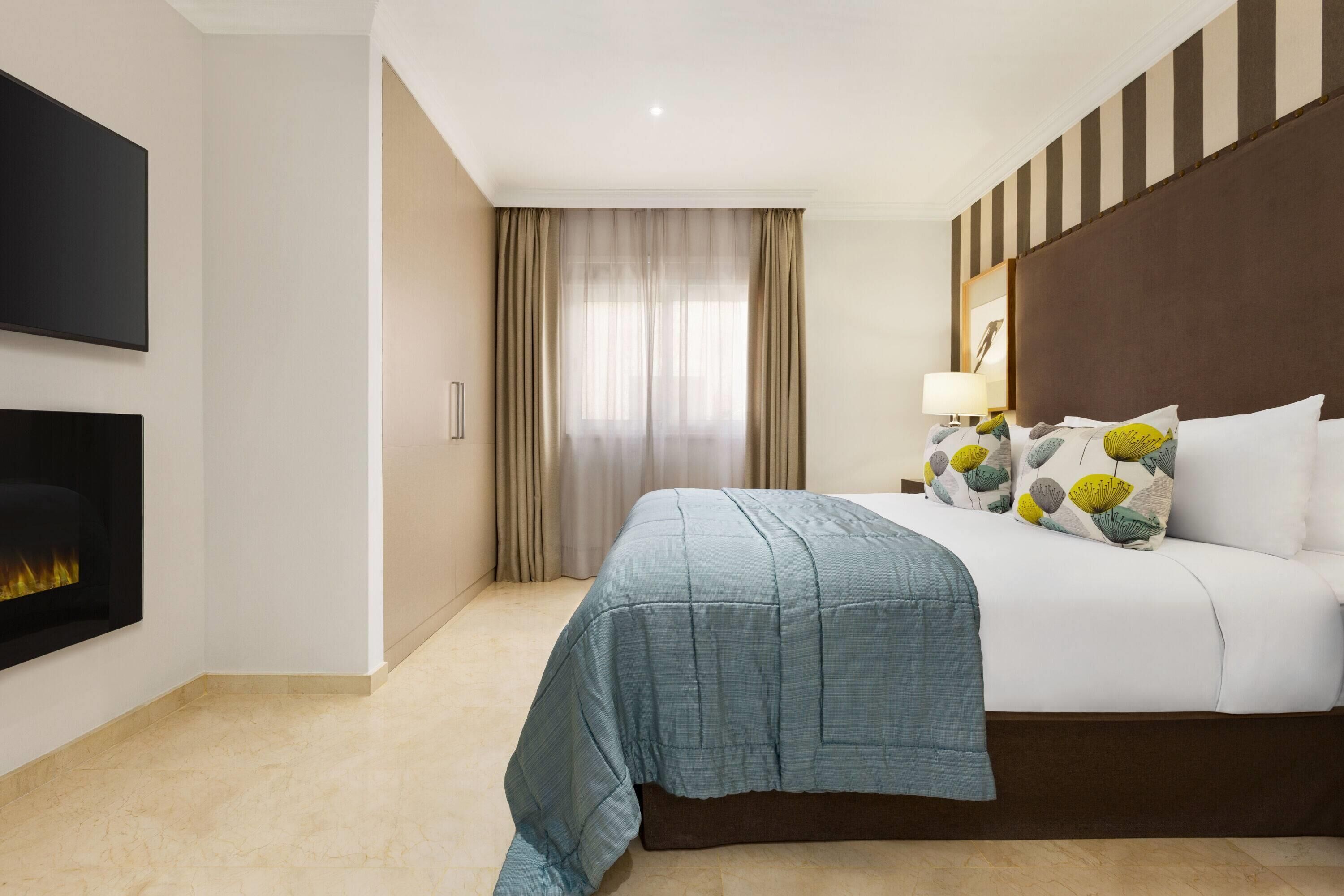 Une chambre d’hôtel équipée d’un lit, d’un téléviseur à écran plat fixé au mur, d’une cheminée et d’une fenêtre avec des rideaux.