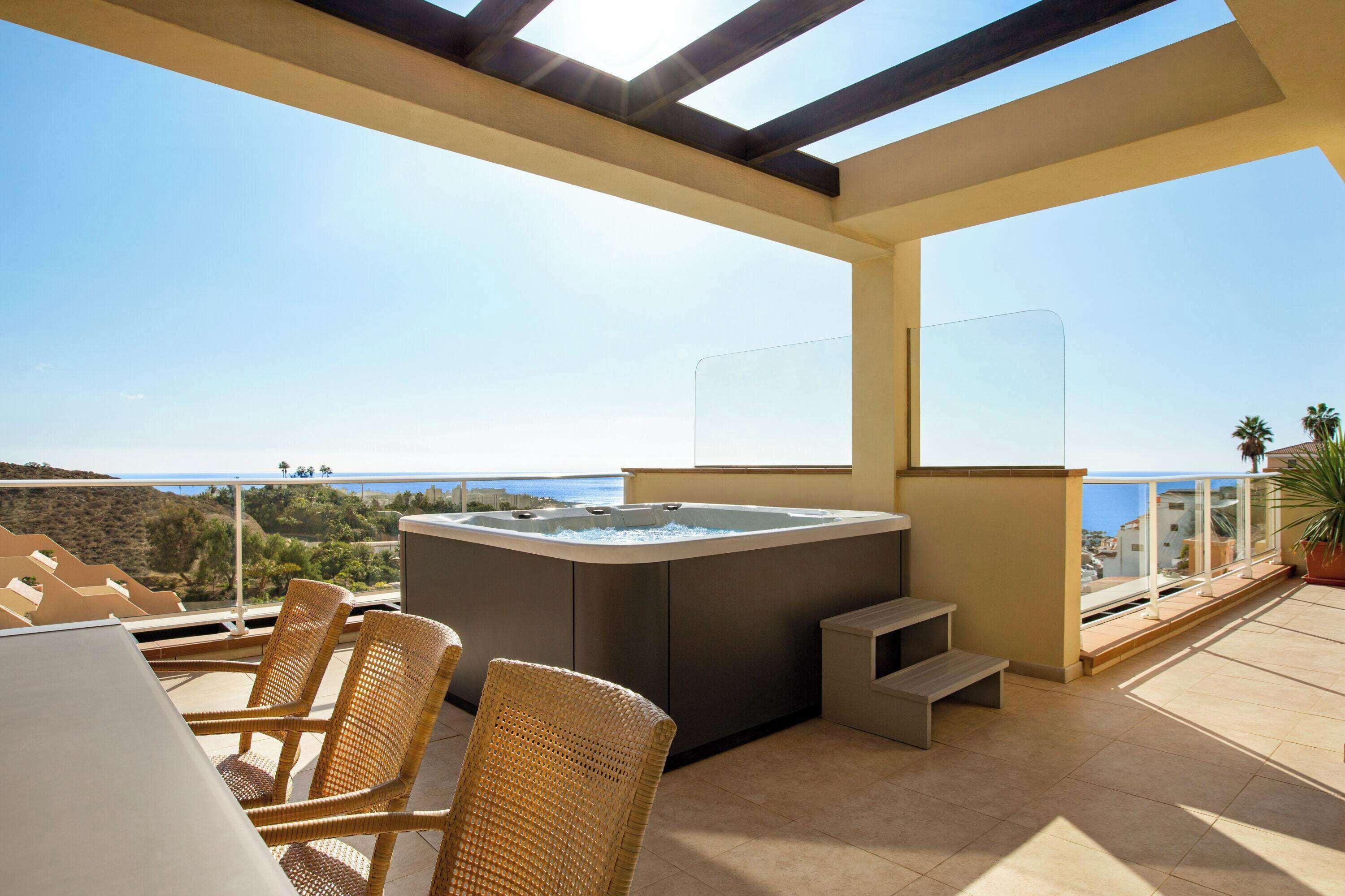 A balcony with a hot tub, wicker chairs, and a view of the sea.