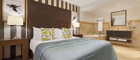 A hotel room with a large bed, two bedside tables with lamps, a bathroom with a sink and mirror, and striped wall decor.
