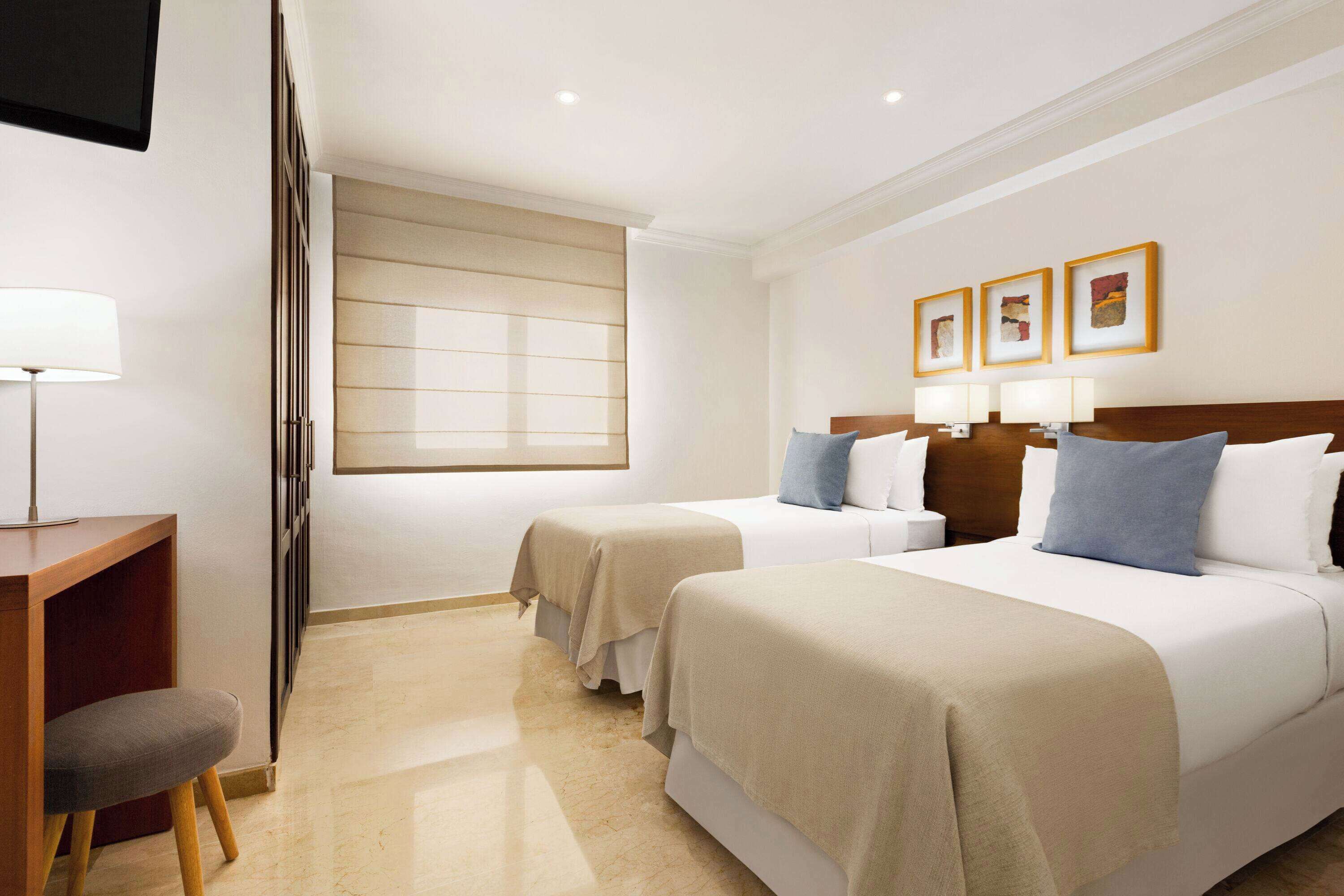 Een hotelkamer met twee bedden, een bureau, een stoel en een raam met zonwering.