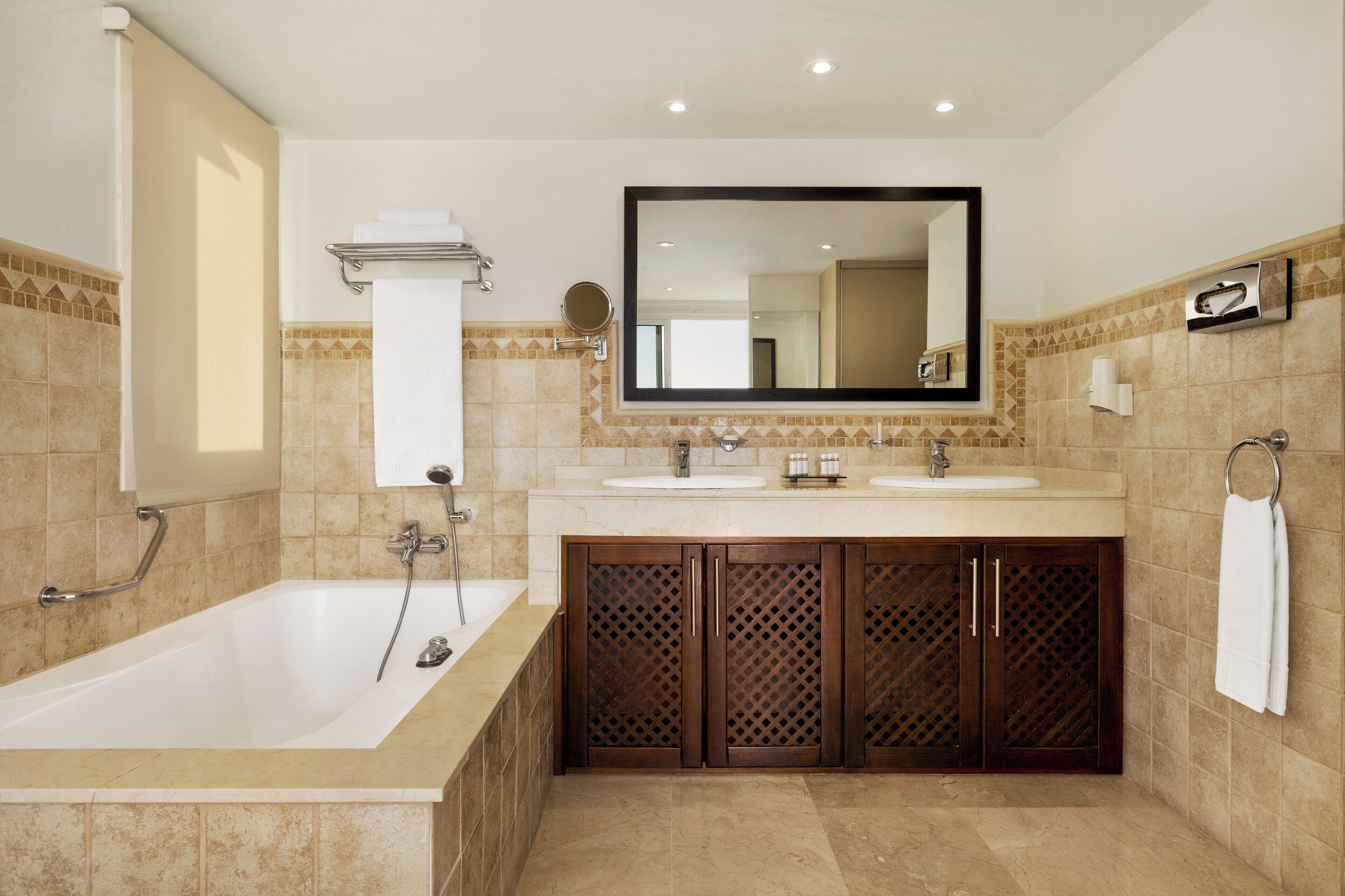 A modern bathroom with a bathtub, two sinks, a large mirror, and a towel rack.