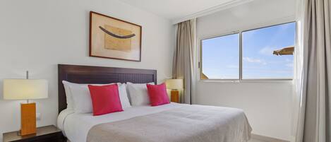 A hotel room with a large bed, two bedside tables with lamps, a framed artwork above the bed, and a window with curtains.