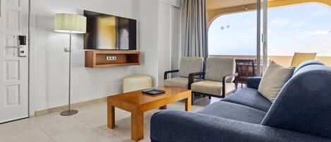 A modern hotel room with a sofa, chairs, a table, a TV, and a sliding door to a balcony.