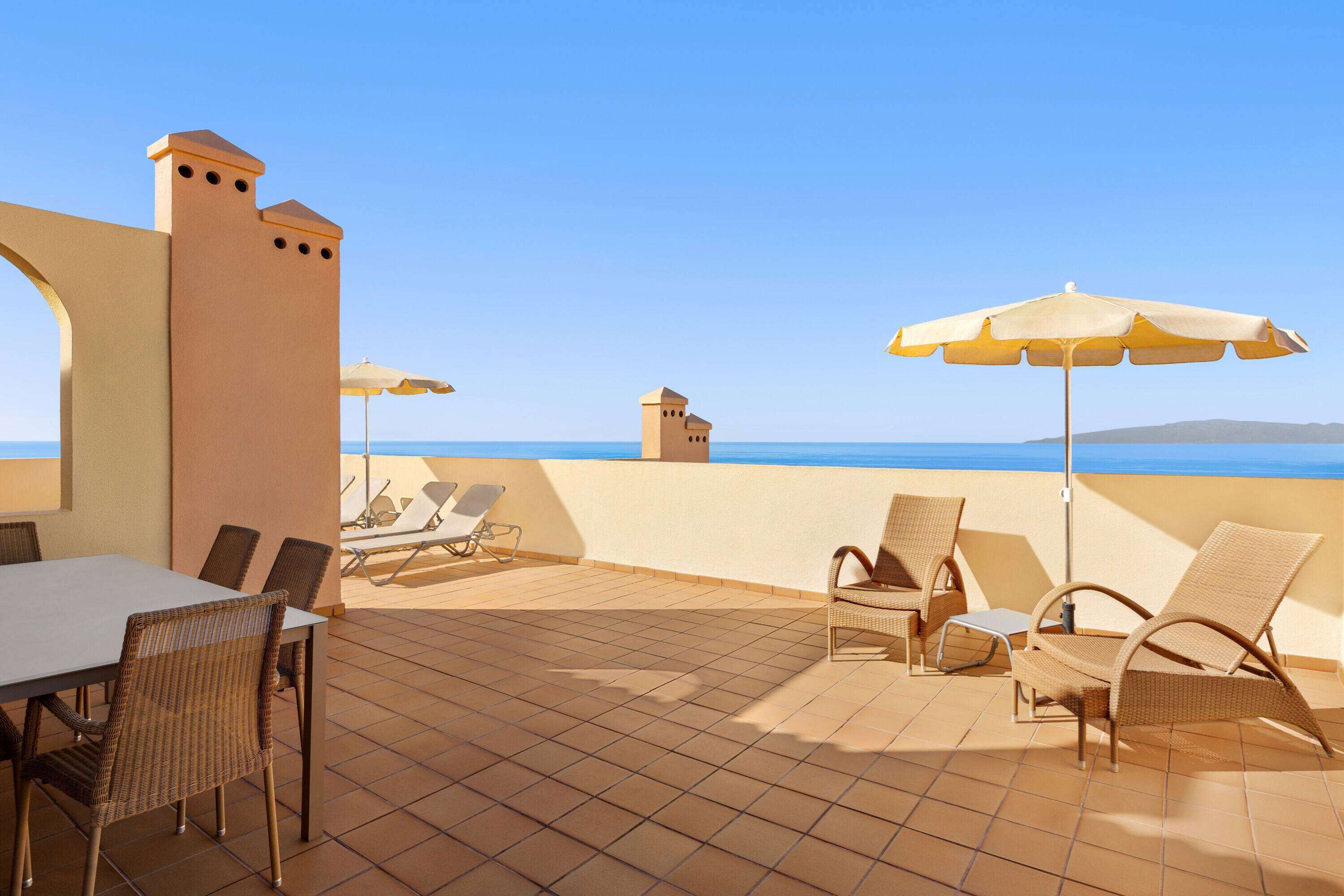 Una terraza con una mesa y sillas, una pequeña torre y vistas al mar.
