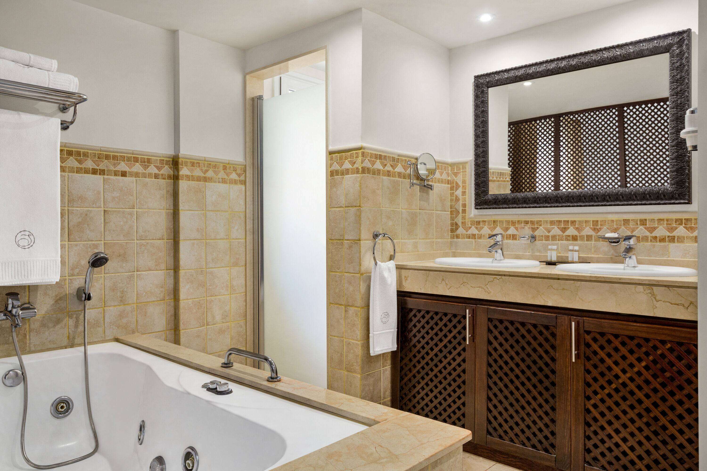 A modern bathroom with a large bathtub, two sinks, and a mirror above the vanity.