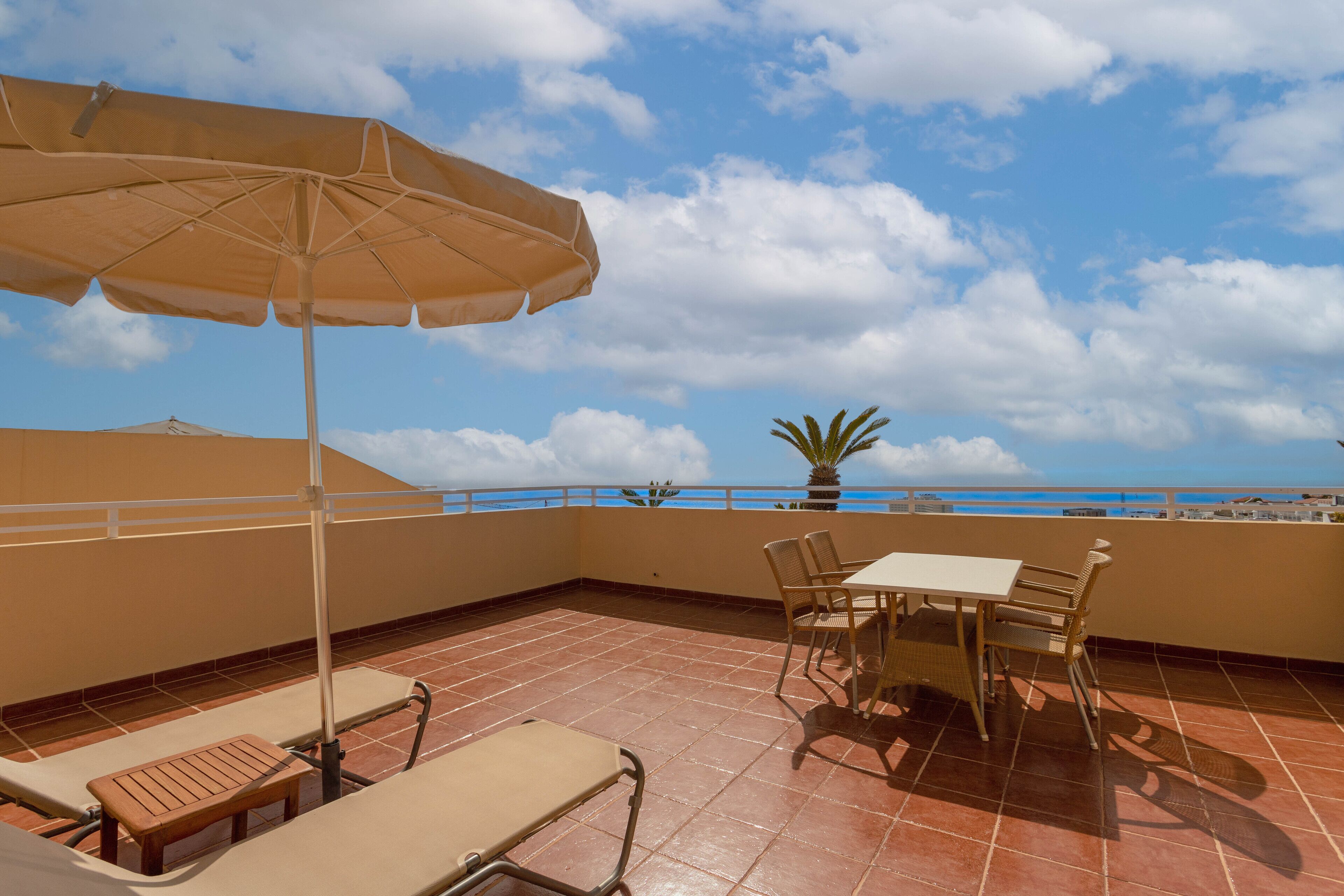 A terrace with a table and chairs, an umbrella, and a view of the sea.