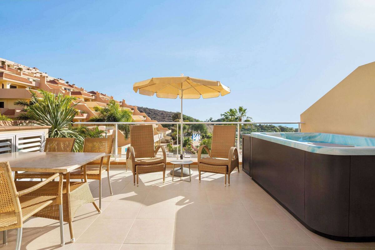A rooftop terrace with a hot tub, wicker furniture, and a view of the surrounding buildings.
