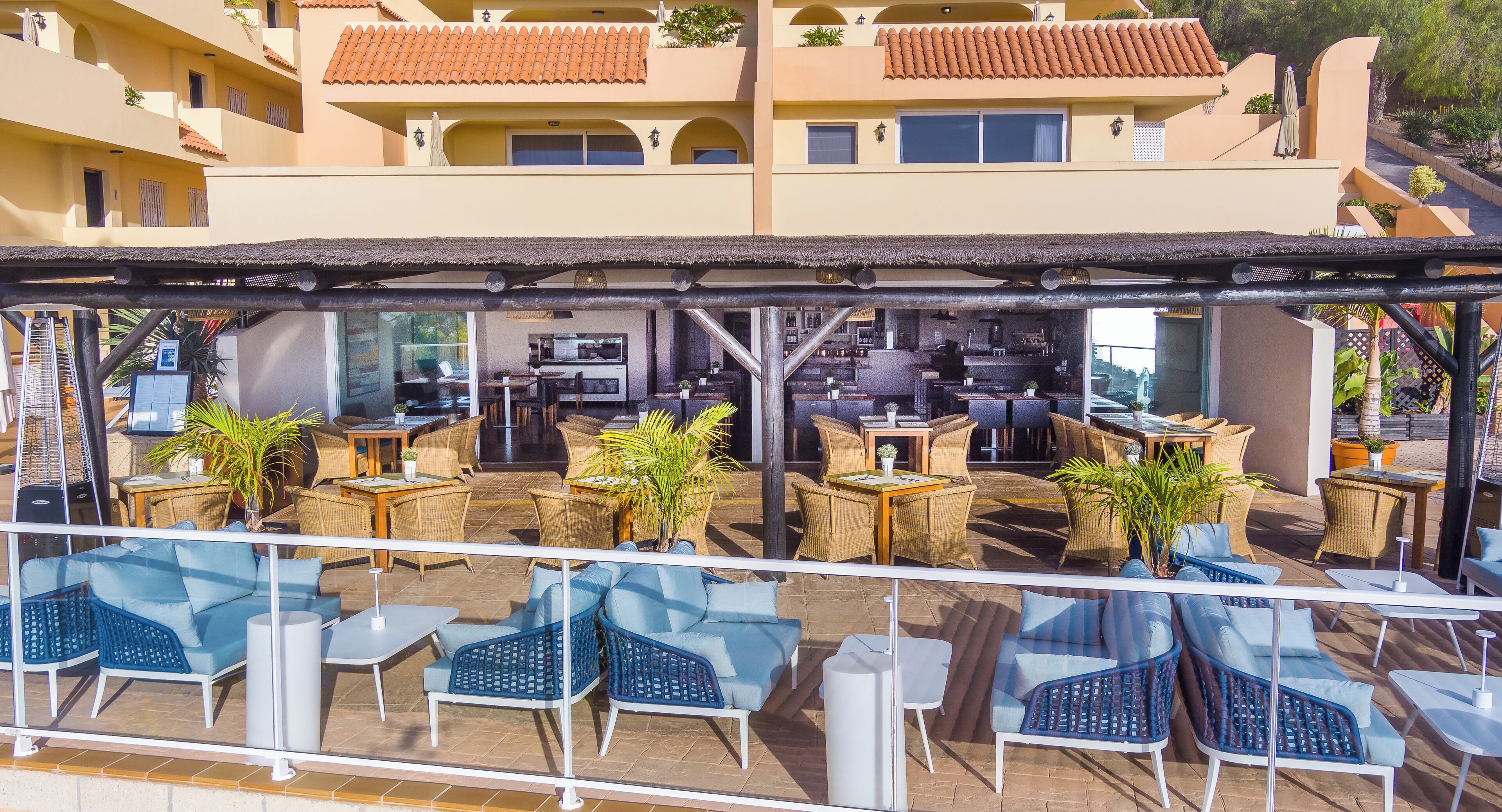 Un patio al aire libre con mobiliario de mimbre, una barra y una cocina visible al fondo.