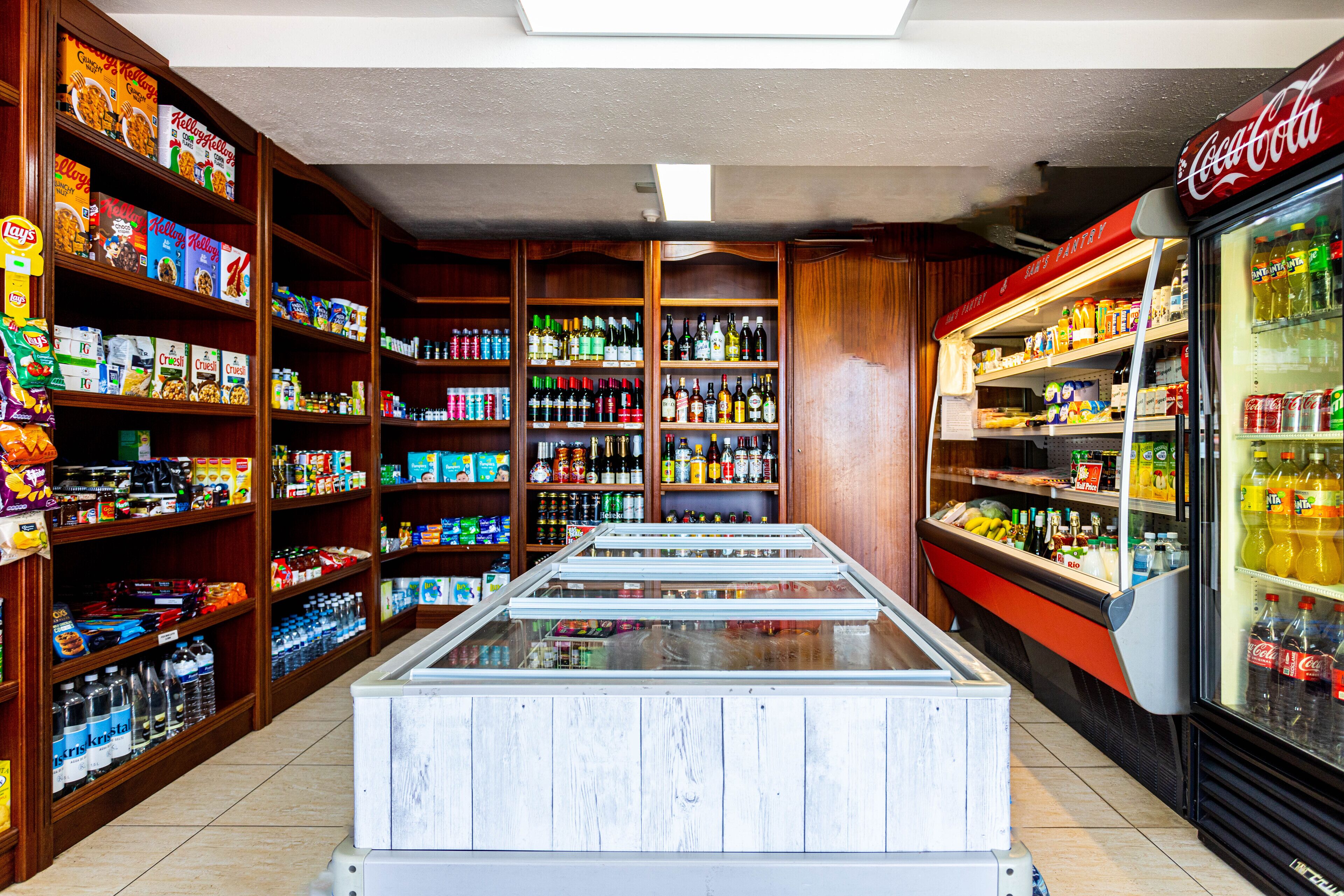 A grocery store with shelves stocked with various products, a refrigerated display case, and a Coca-Cola refrigerator.