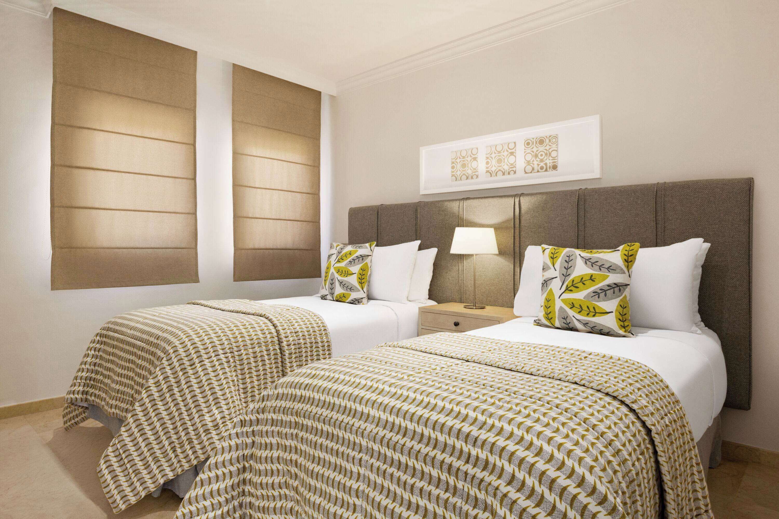 A hotel room with two beds, a nightstand, a lamp, and a framed artwork on the wall.