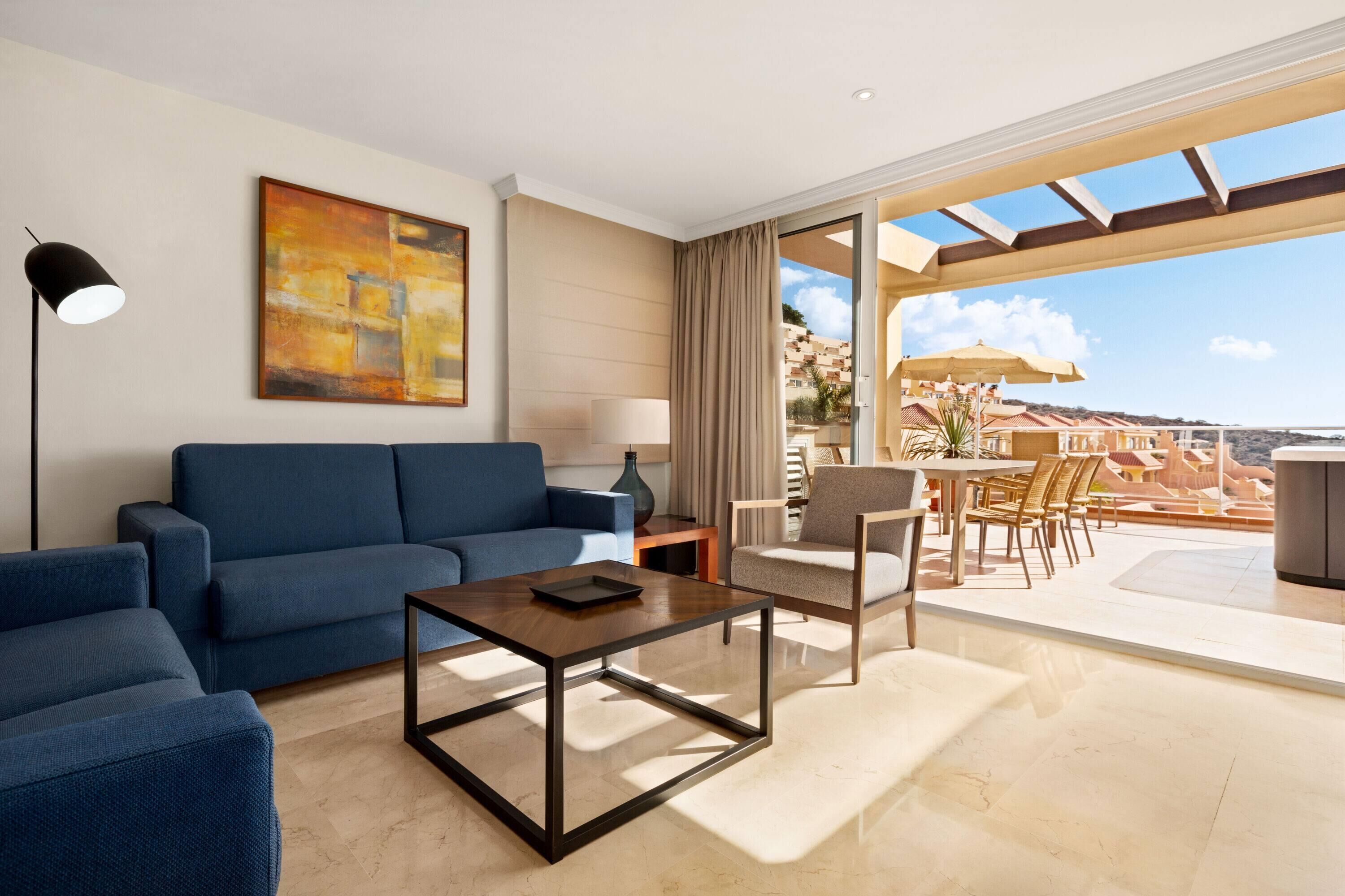 Un hotel moderno con un sofá azul, una mesa de centro de madera y un amplio ventanal con vistas a la ciudad.